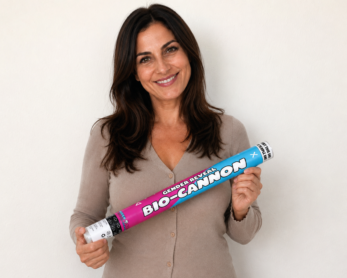 A smiling woman holding a pink and blue Gender Reveal Ideas Bio-Cannon horizontally, photographed against a clean off-white studio background.